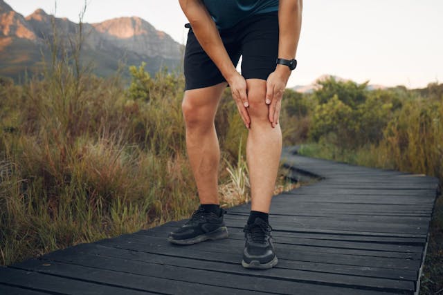 man clutching knee on trail