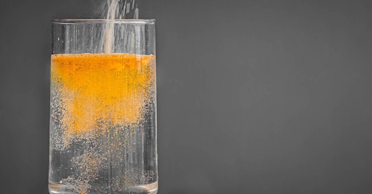 Orange colored sweetener being poured into a glass of water