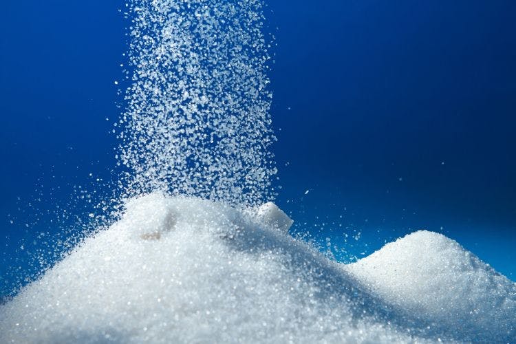 sugar being poured onto a mound of sugar on blue background