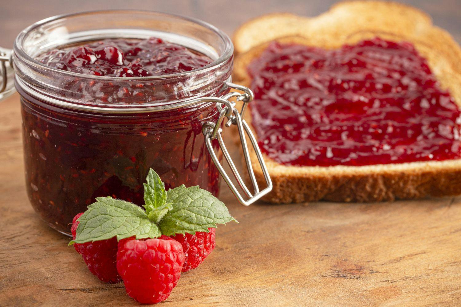 jar of raspberry, jam spread on bread, and three raspberry fruits