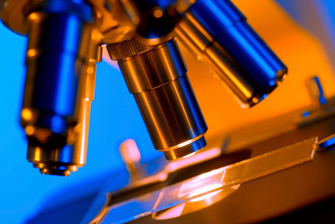 close up of microscope with slide, bathed in orange and blue light