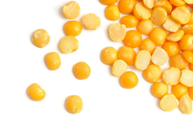 dry yellow peas scattered on white background, accumulating in top right hand corner