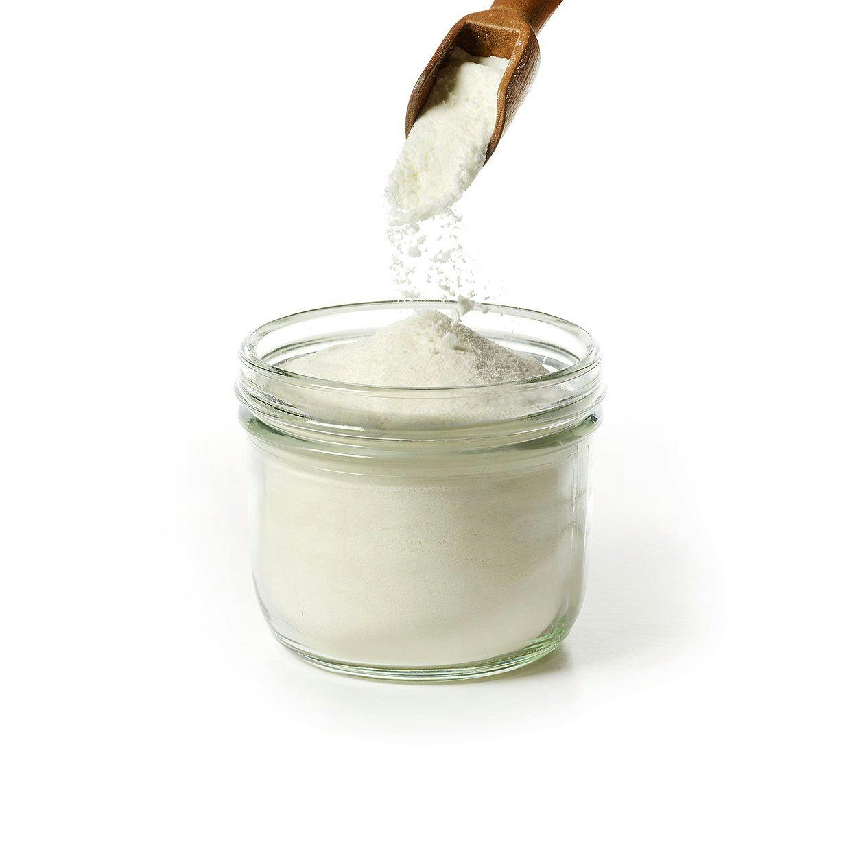 Glass jar filled with white powder. Wooden spoon above jar pours white powder into jar.