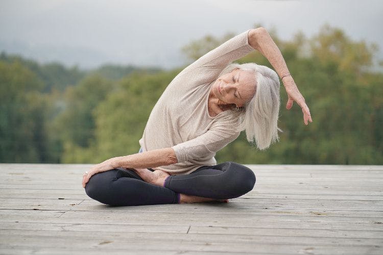 older woman doing yoga on deck outdoors