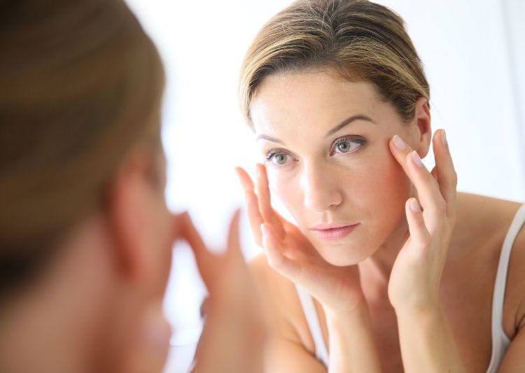 woman looking in the mirror and touching face with fingertips