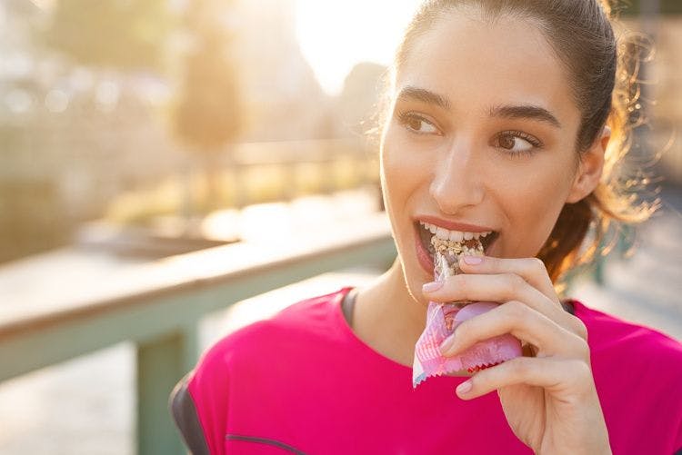 woman wearing pink, eating bar at golden hour