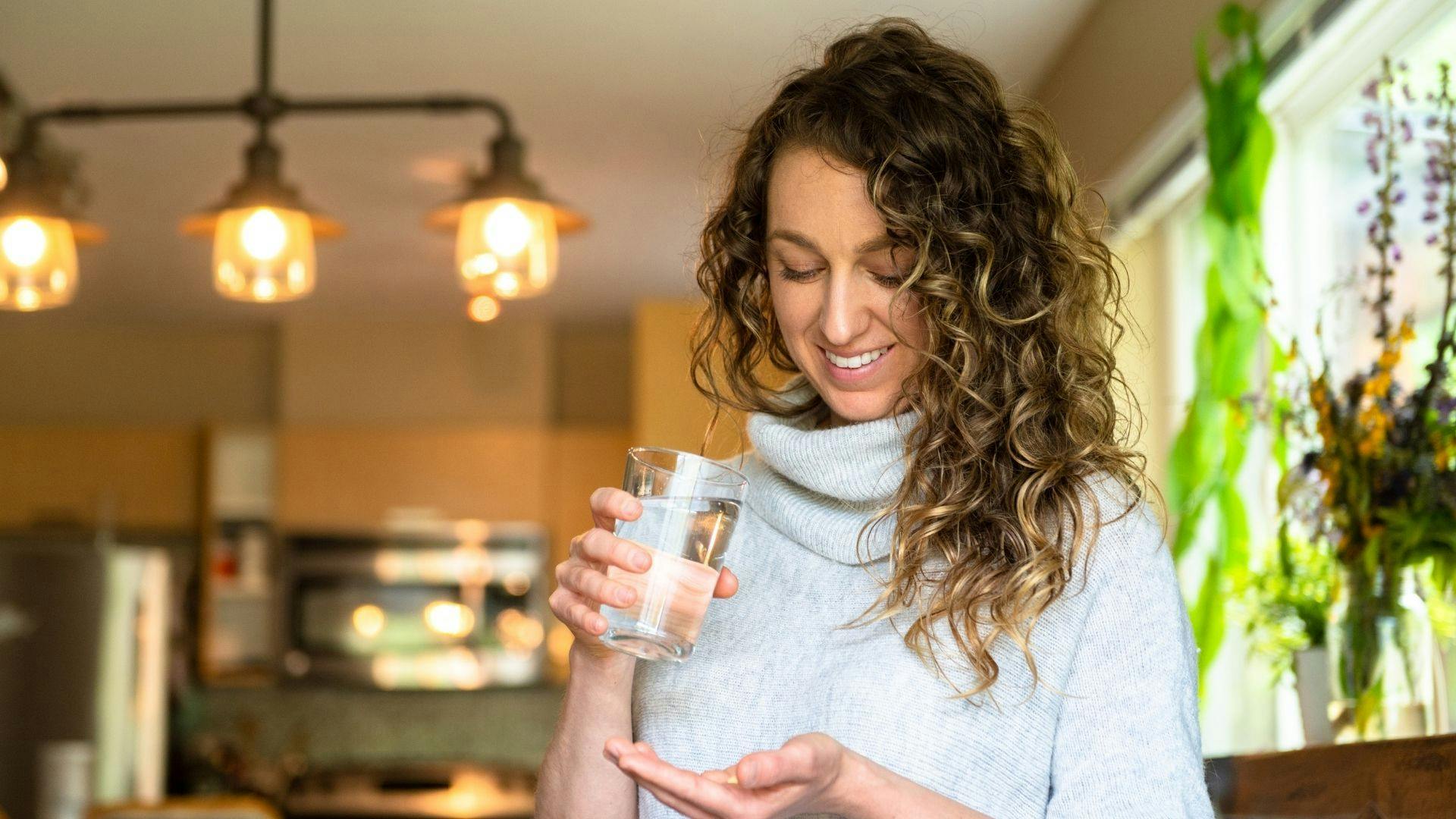 woman holding glass of water, about to take a dietary supplement