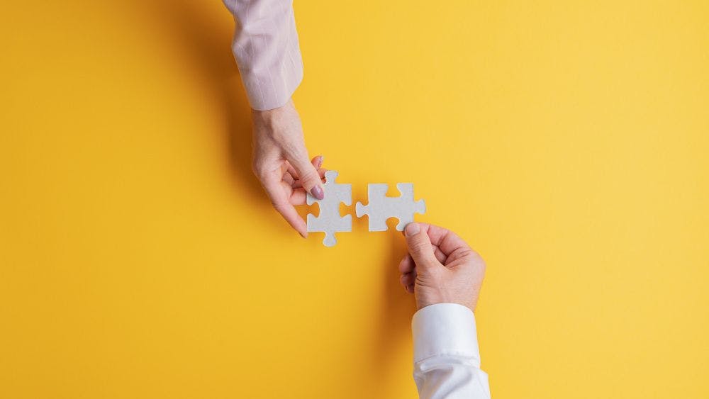 two hands putting puzzle pieces together on yellow background