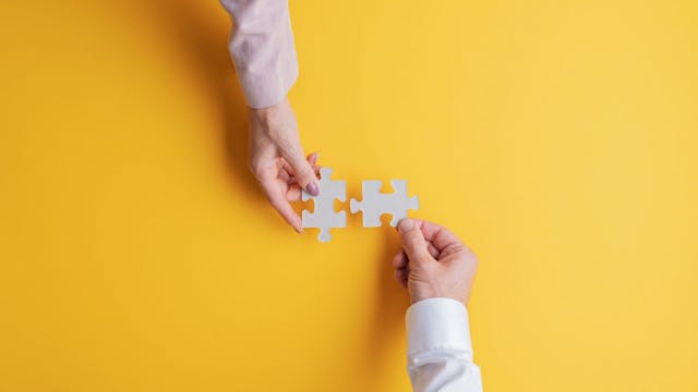 two hands putting puzzle pieces together on yellow background