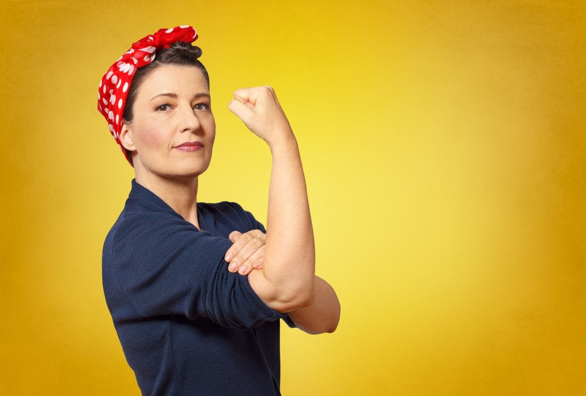 middle aged woman flexing bicep dressed as Rosie the riveter