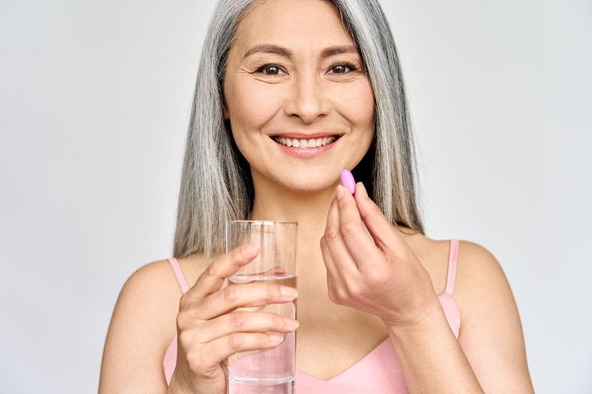 older woman smiling at camera, taking supplement and holding glass of water