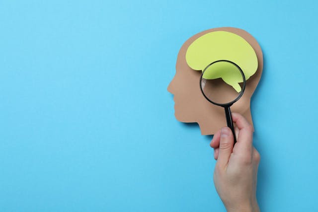 hand holding magnifying glass over a paper cutout of head and brain