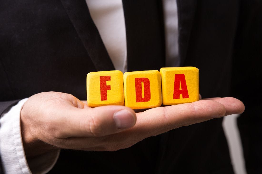 Yellow blocks spelling FDA in a man's open hand